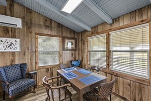 A room with wooden walls, a dining table with blue placemats, and a blue patterned sofa. - Warblers Roost- Bird Watcher Paradise | Great view (Crystal Beach)