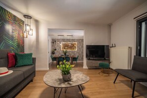 A modern living room with a sofa, a round coffee table with a plant, a dining area with chairs, a TV, and a fireplace. - Villa Casa del Miele - Holidays in Crete (Skonízo)