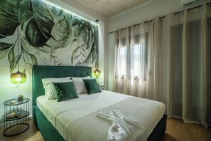 A neatly made bed with a green headboard, a small bedside table with a plant, and a wall with a leaf pattern. - Villa Casa del Miele - Holidays in Crete (Skonízo)