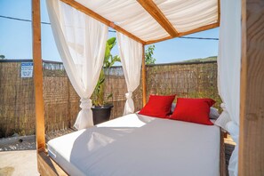 A bed with white bedding and red pillows in a covered outdoor area with a bamboo fence in the background. - Villa Casa del Miele - Holidays in Crete (Skonízo)