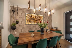 A dining area with a wooden table, green chairs, hanging pendant lights, a stone wall, and a vintage sewing machine. - Villa Casa del Miele - Holidays in Crete (Skonízo)