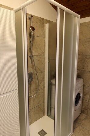Eine begehbare Dusche mit Glastür, Duschkopf und integrierter Waschmaschine.