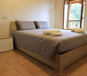 A bedroom with a bed, a nightstand, and a window with a view of greenery. - Botton D'oro - One Bedroom Apartment, Sleeps 4 (Teveno)