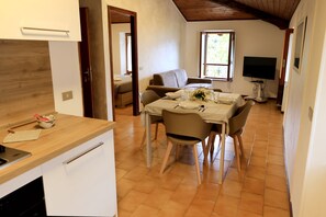 A dining area with a table set for four, a sofa, and a television in the background. - Botton D'oro - One Bedroom Apartment, Sleeps 4 (Teveno)