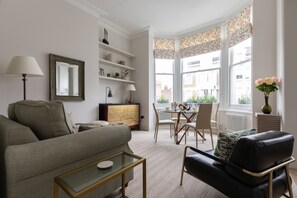 Una sala moderna con un sofá, una mesa de centro de vidrio, un sillón de cuero, un comedor con mesa y sillas, y vista a la ciudad a través de amplios ventanales.