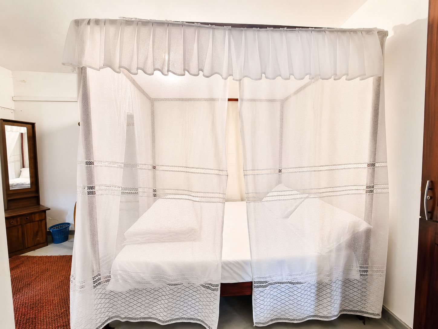 Una habitación con una cama bajo un dosel, un aparador de madera y un cuadro en la pared.