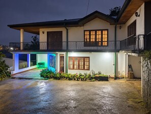 A two-story house with a balcony, a covered patio, and a garden area with potted plants.