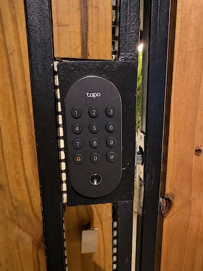 A black electronic keypad with the brand 'tapo' mounted on a wooden door frame.