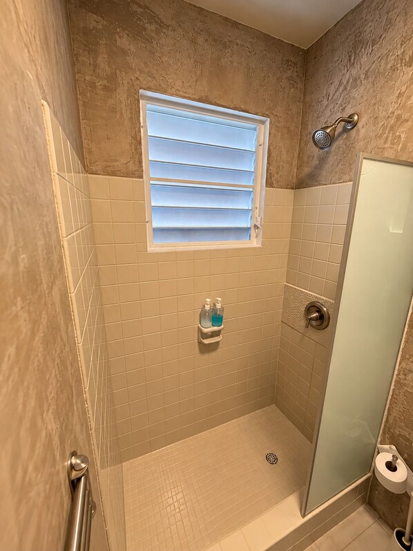 A small bathroom with a shower, a window, and a toilet.