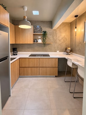 A modern kitchen with wooden cabinets, a central island, bar stools, a coffee maker, a clock, and a globe.