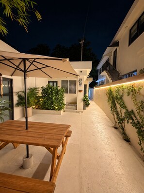 An outdoor patio area with a wooden table and chairs, surrounded by potted plants and a wall with climbing plants.