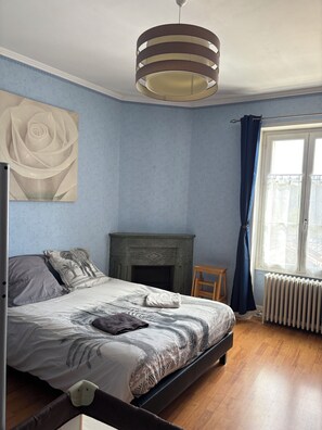 Ein Schlafzimmer mit Bett, Kamin, Heizkörper, einem Fenster mit Vorhängen und einer Deckenleuchte.