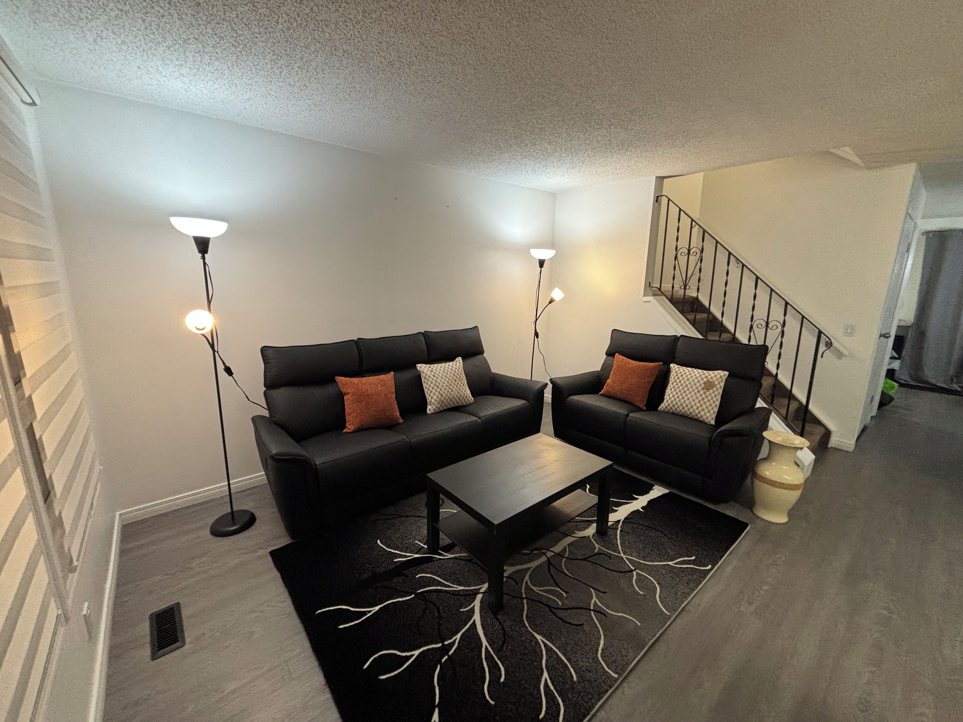 A modern living room with two black sofas, a coffee table, and two floor lamps.