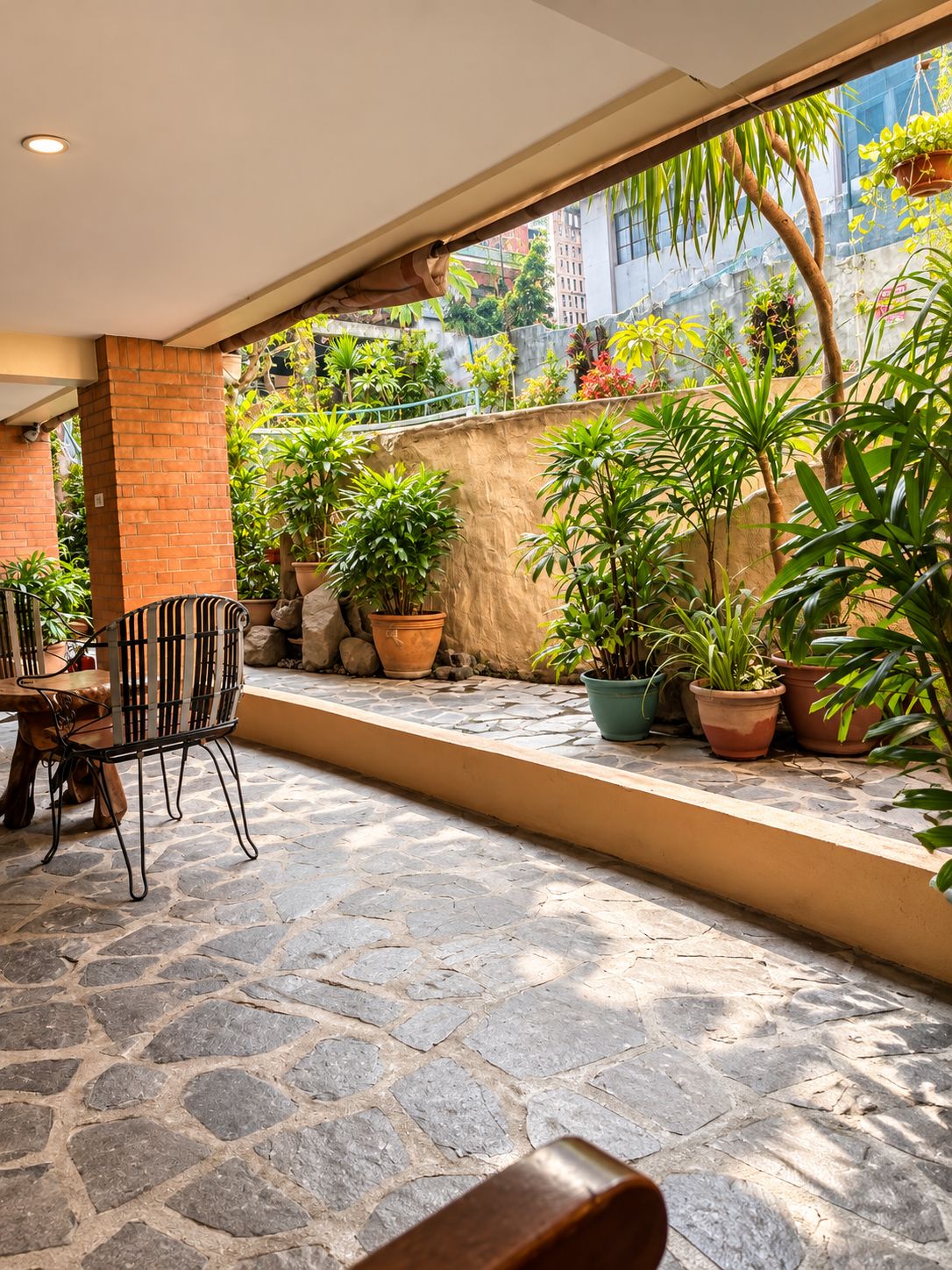 An outdoor patio area with a stone floor, a table with chairs, and various potted plants.