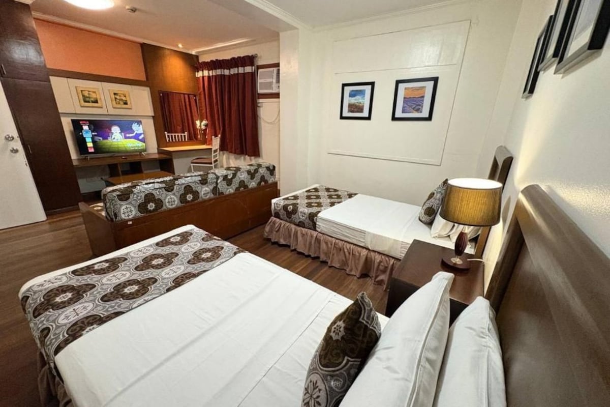 A hotel room with two beds, a TV, a desk, and a chair.