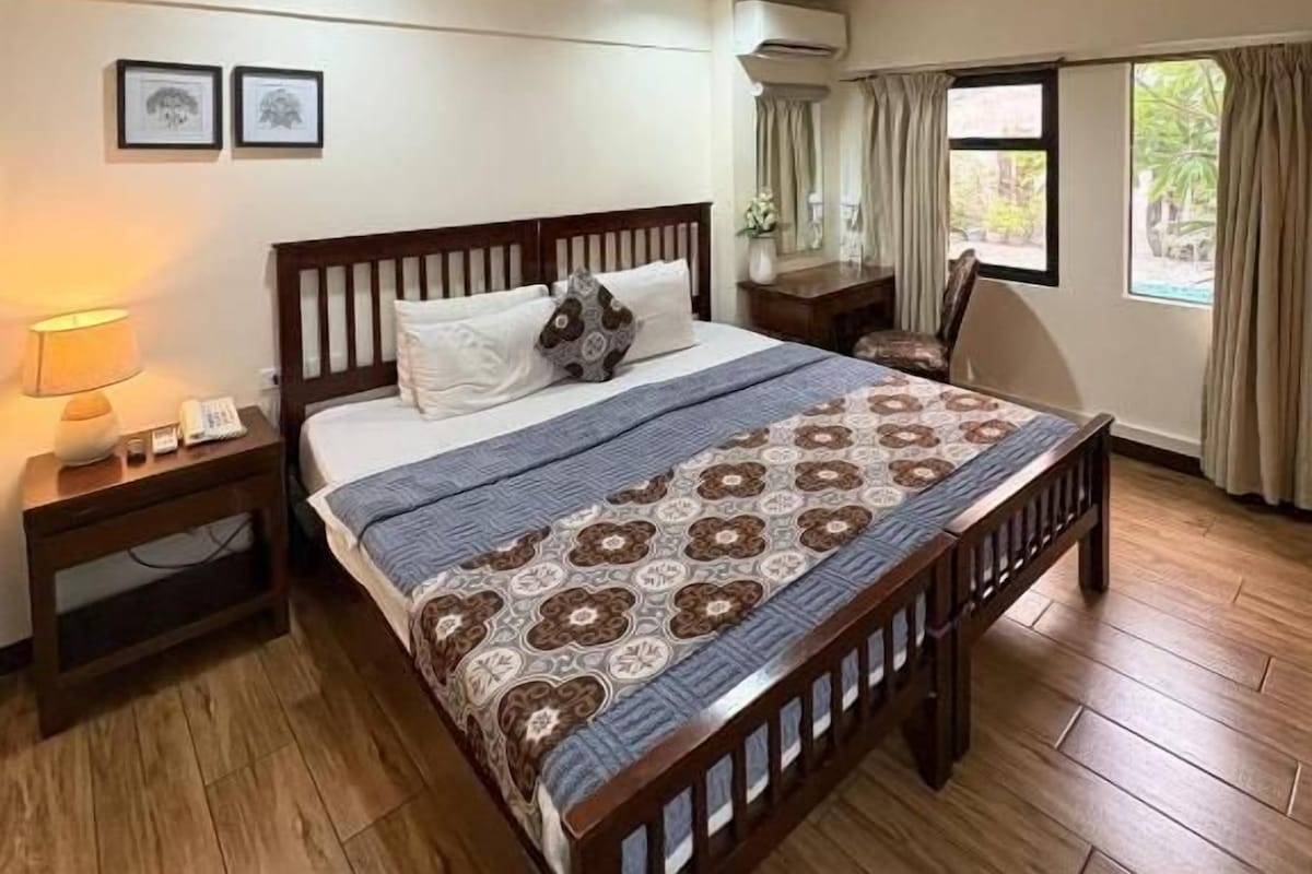 A bedroom with a wooden bed, bedside tables, a lamp, and a window with curtains.