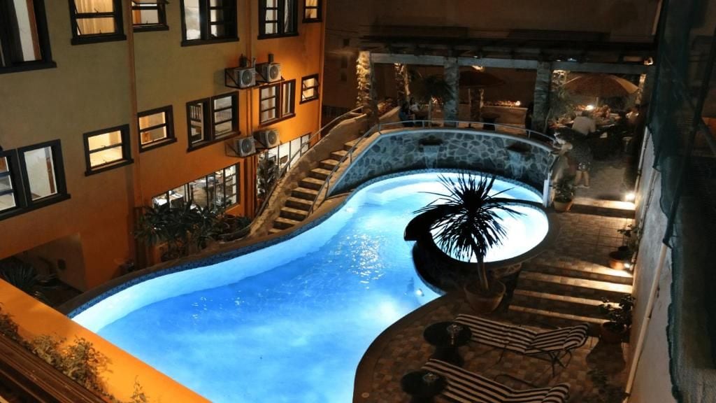 Una piscina de diseño curvo, rodeada por un muro de piedra y escalones que conducen a una zona de estar exterior con sombrillas.