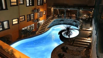 Una piscina de diseño curvo, rodeada por un muro de piedra y escalones que conducen a una zona de estar exterior con sombrillas.