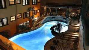 A swimming pool with a curved design, surrounded by a stone wall and steps leading to an outdoor seating area with umbrellas. - 1775 Adriatico Suites (Manila)