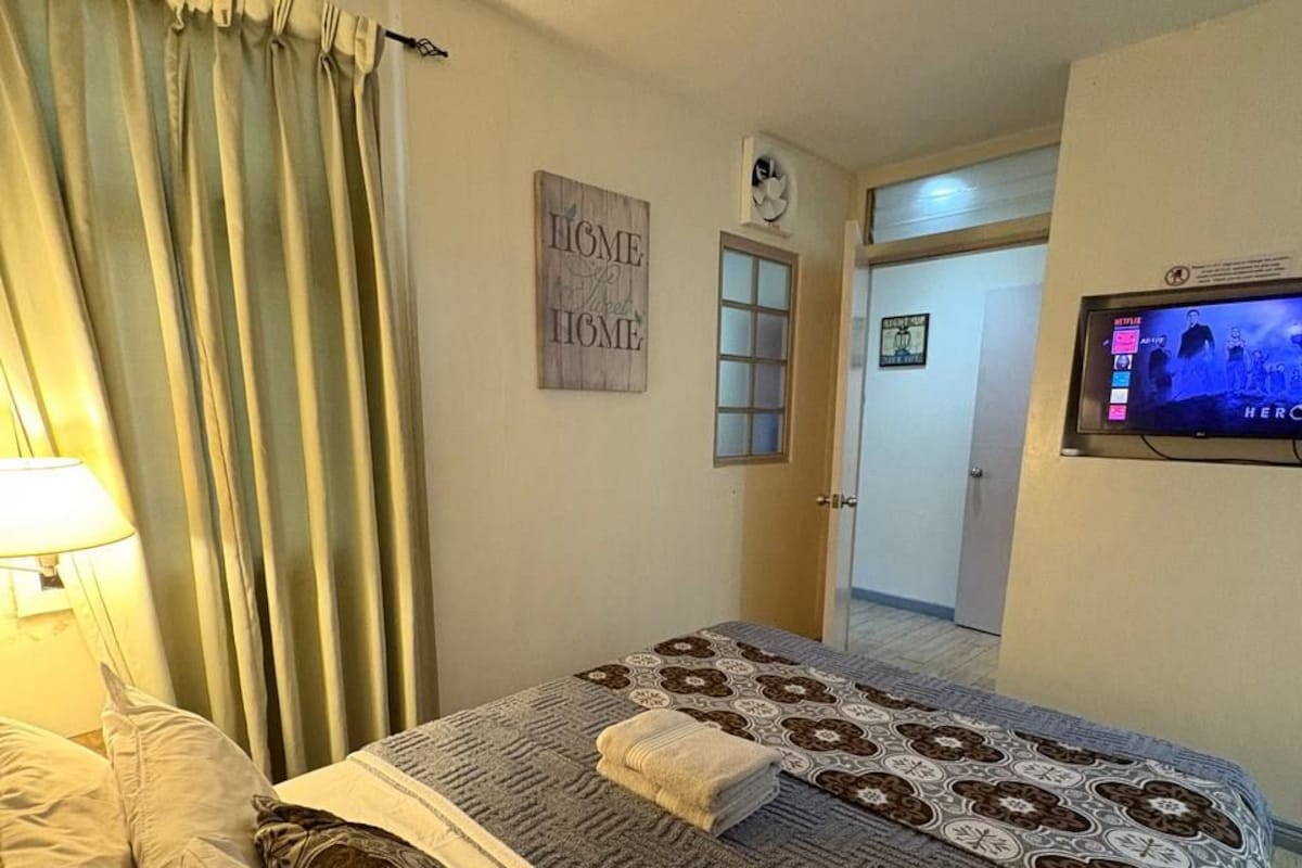 A hotel room with a bed, a TV, a door, and a wall-mounted sign.