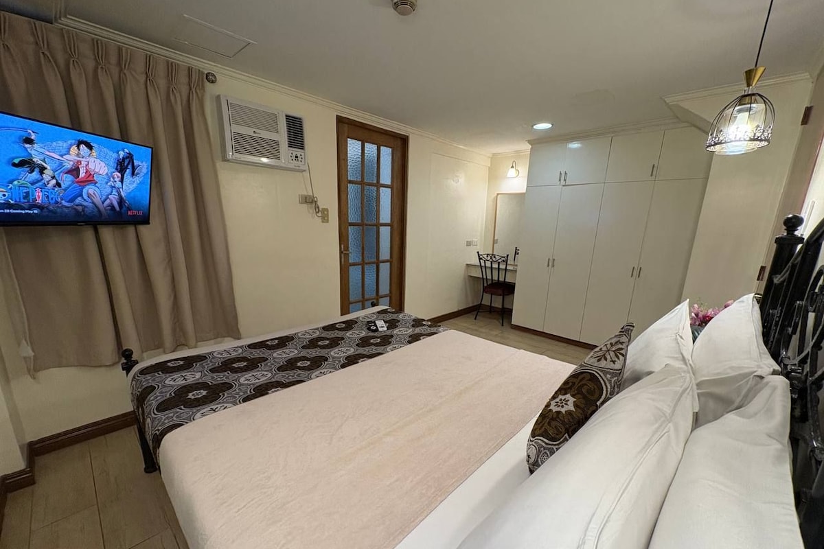 A bedroom with a bed, a television, a wardrobe, and a dining area.