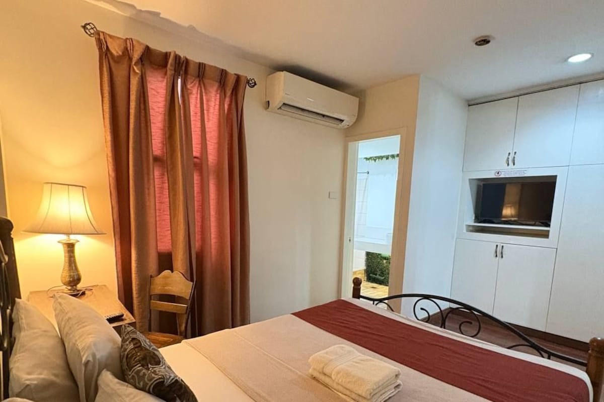 A hotel room with a bed, a desk, a lamp, a TV, and a kitchenette.