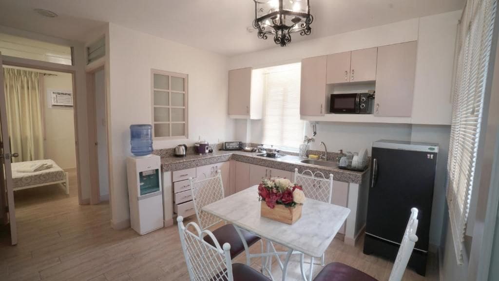 A compact kitchen with a dining table, chairs, a water dispenser, a microwave, and a refrigerator.