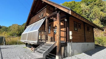 Une cabane en bois dotée d’un porche couvert, d’un escalier menant à l’entrée et d’une allée gravillonnée.
