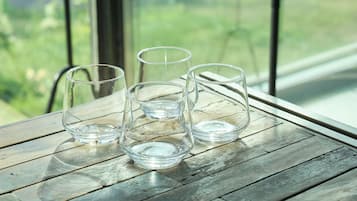 Quatre verres à boire en verre transparent, posés sur une table en bois, avec vue sur la verdure à travers une fenêtre.