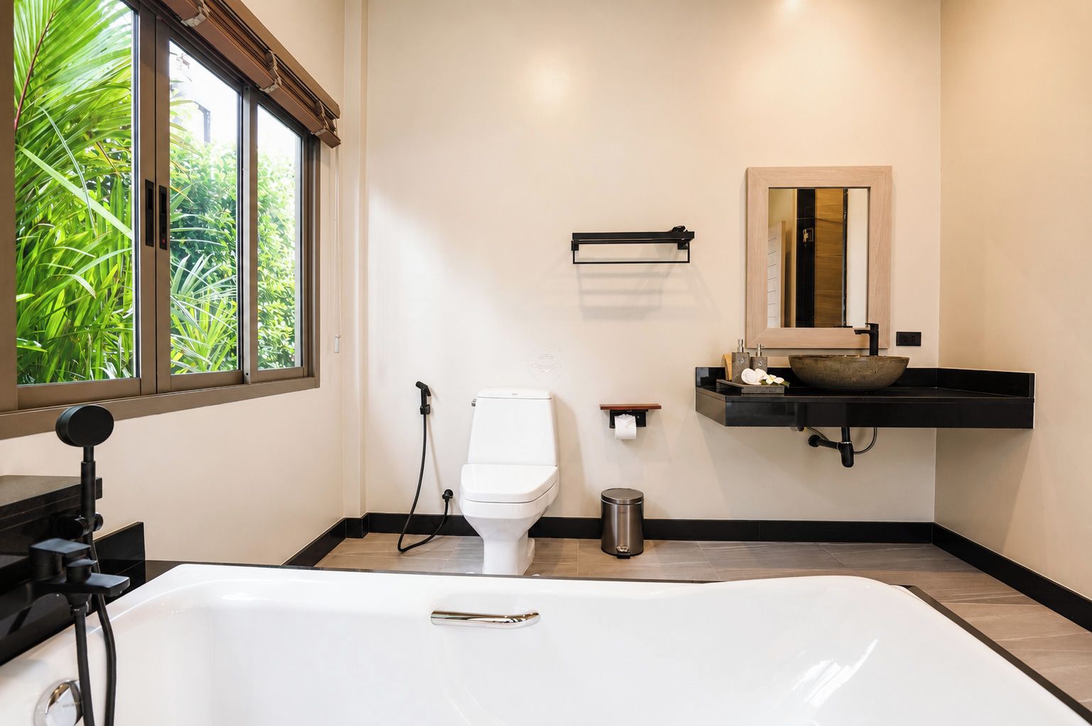 A modern bathroom with a large bathtub, a toilet, and a sink with a mirror above it.