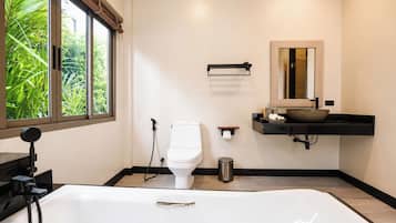 A modern bathroom with a large bathtub, a toilet, and a sink with a mirror above it.