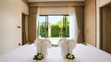 A hotel room with a large bed, two towels arranged in a decorative manner, and a view of a pool and greenery outside.