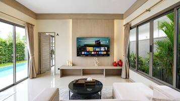 A modern living room with a flat-screen TV mounted on the wall, a glass coffee table, and a sofa.