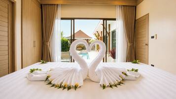 A hotel room with a bed, two swan-shaped towels, and a view of a pool and outdoor area.