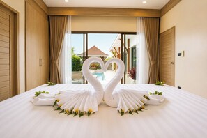 A hotel room with a bed, two swan-shaped towels, and a view of a pool and outdoor area.