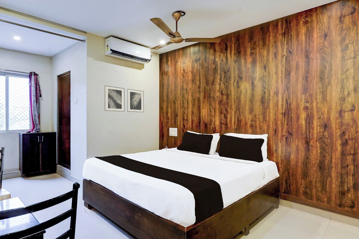 A bedroom with a wooden panel wall, a bed with white and black bedding, a ceiling fan, and an air conditioning unit.