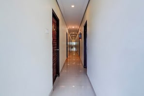 A long, narrow hallway with doors on both sides, a fire extinguisher on the right wall, and a light fixture on the ceiling.
