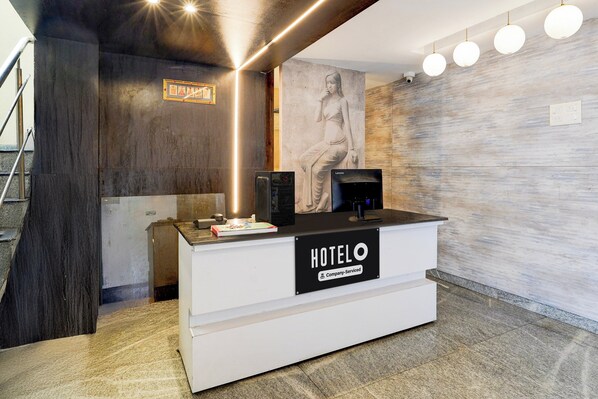A hotel reception desk with a 'HOTELO' sign, a framed picture above it, and a statue on the wall.