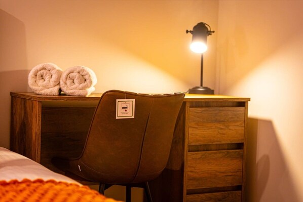 Un bureau en bois, une chaise, une lampe et deux serviettes enroulées.