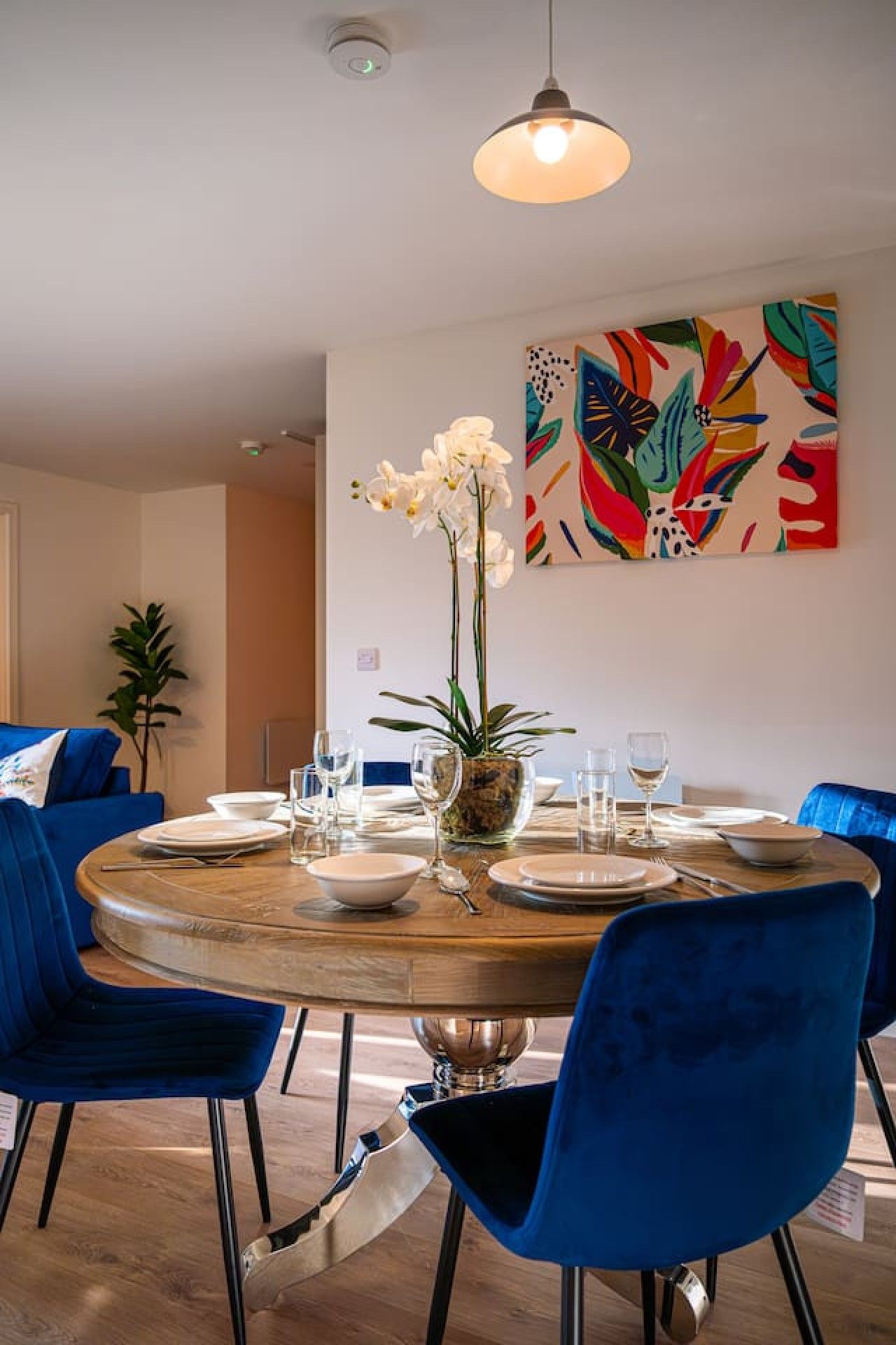 A dining area with a round table, blue chairs, and a potted plant.