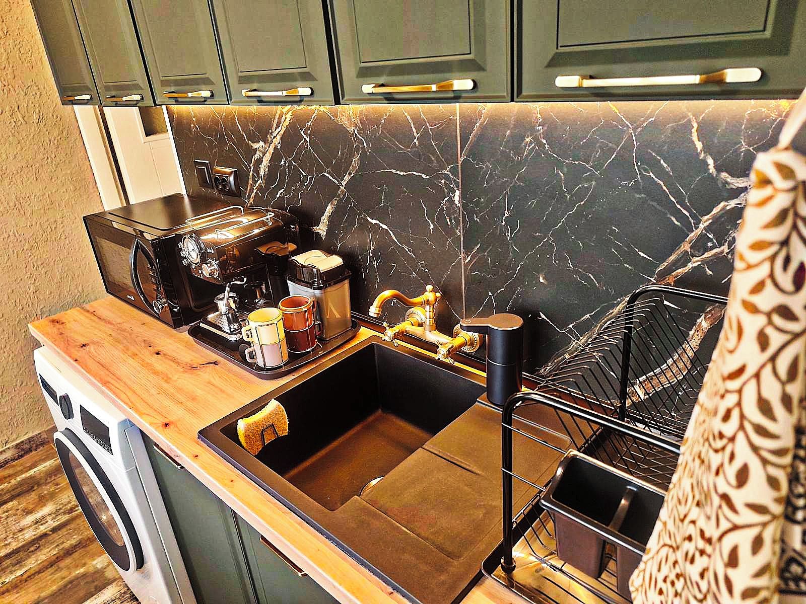 A kitchen with a marble backsplash, a coffee machine, a sink, and a dish rack.