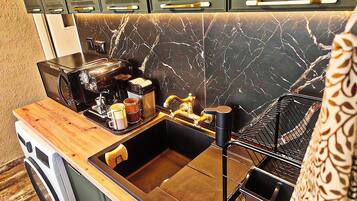 A kitchen with a marble backsplash, a coffee machine, a sink, and a dish rack.