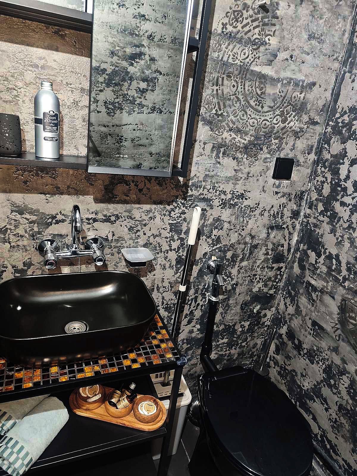 Casa de banho com lavatório preto, espelho, chuveiro e parede estampada.