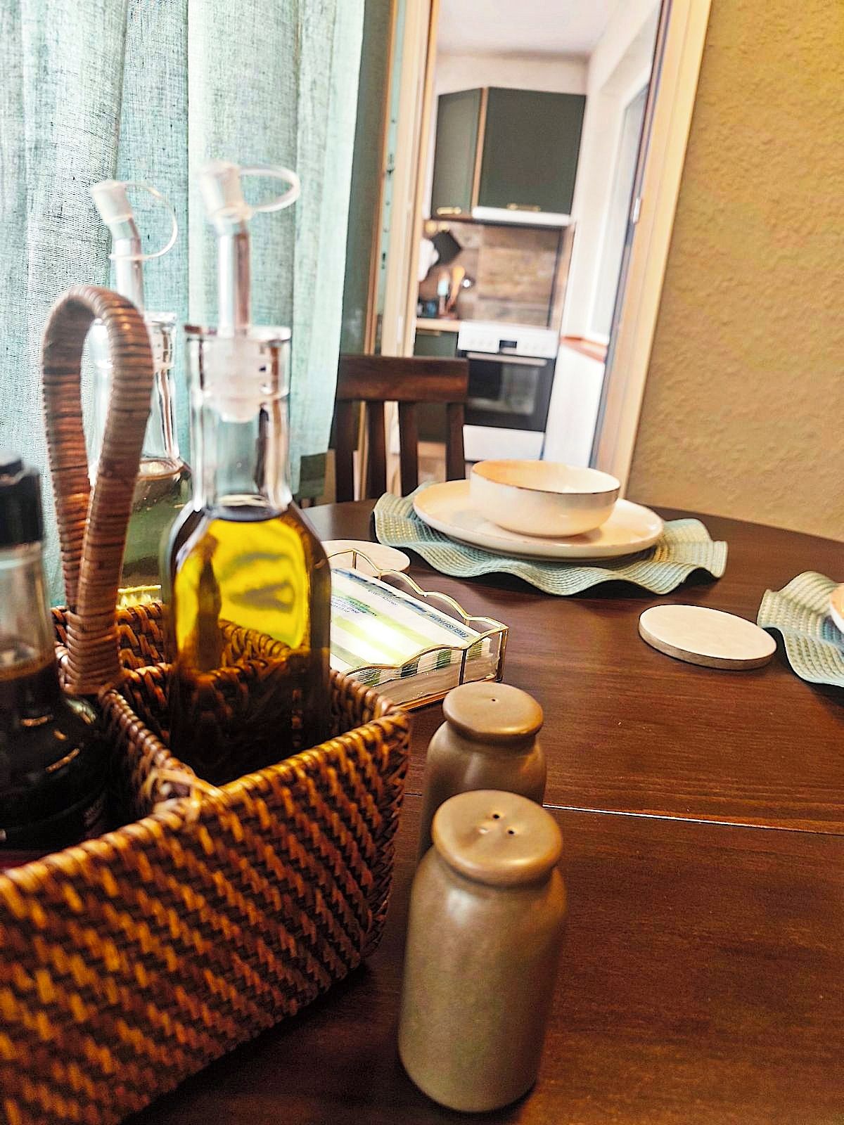 Une table à manger sur laquelle se trouve un panier en osier contenant une bouteille, des salières et des poivrières, ainsi qu’une assiette avec un bol.