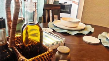 Une table à manger sur laquelle se trouve un panier en osier contenant une bouteille, des salières et des poivrières, ainsi qu’une assiette avec un bol.