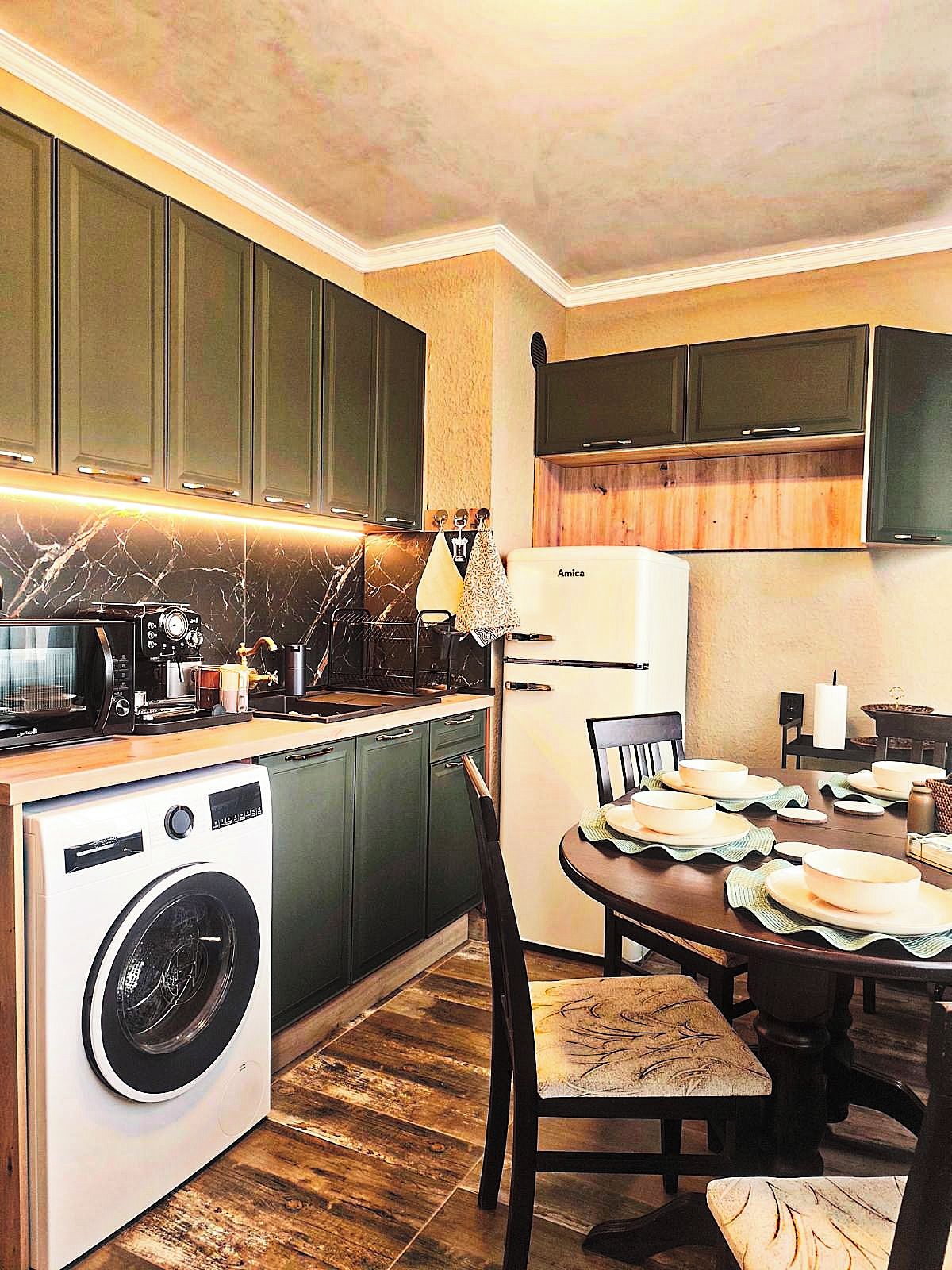 Una cocina funcional con lavadora, una mesa de comedor con sillas y un refrigerador.