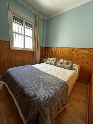 A bedroom with a bed, wooden paneling, a window with bars, and a curtain. - New Listing (Barbate)