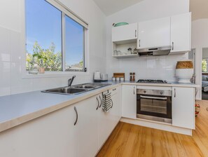 A modern kitchen with white cabinetry, a stainless steel sink, and a built-in oven. - Pottsville Coastal Retreat (Pottsville)