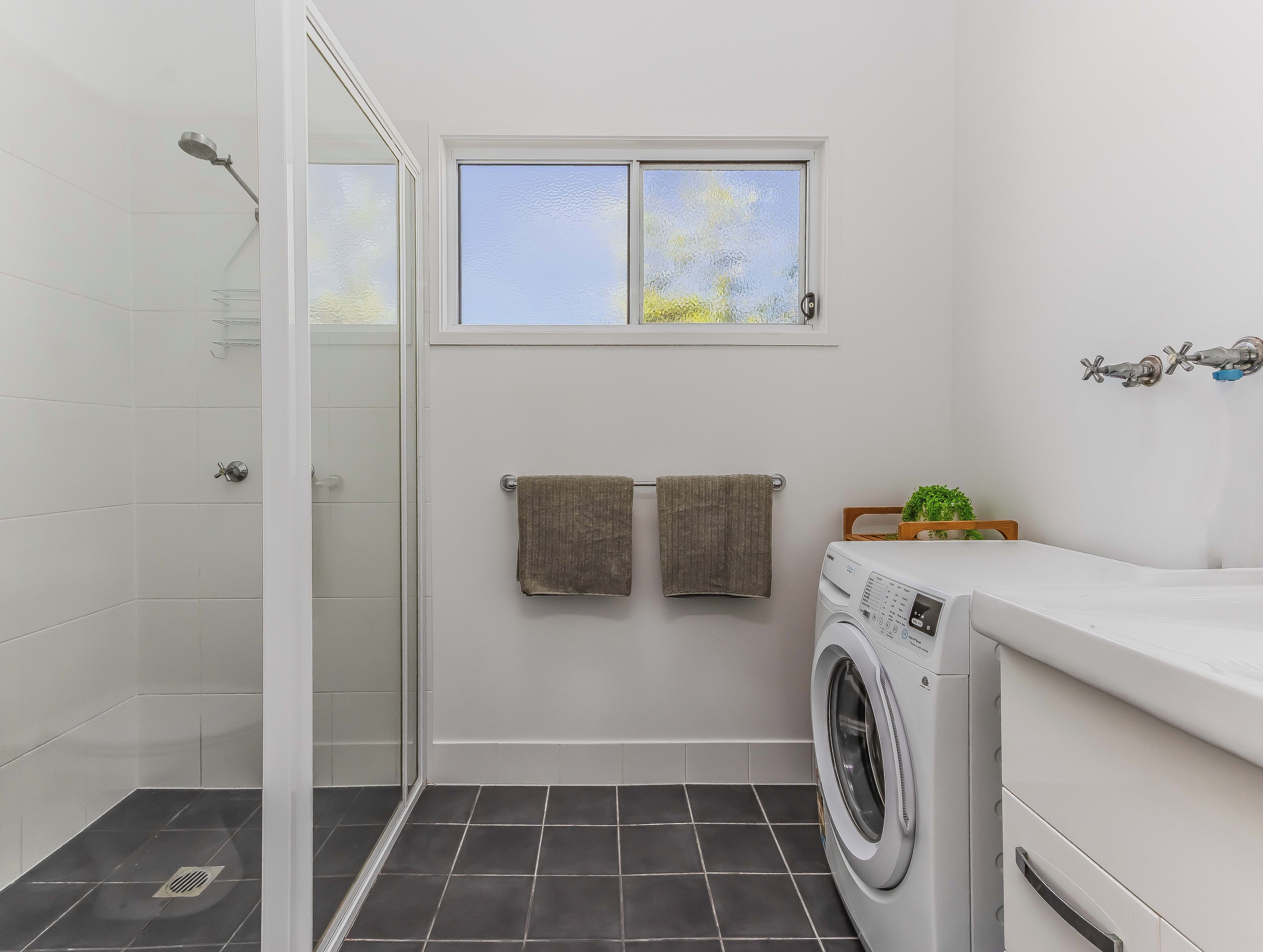 A compact bathroom with a shower, a window, a washing machine, and a towel rack.