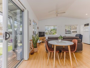 A modern living room with a glass door leading to a balcony, a dining area with a table and chairs, a sofa, and a television.